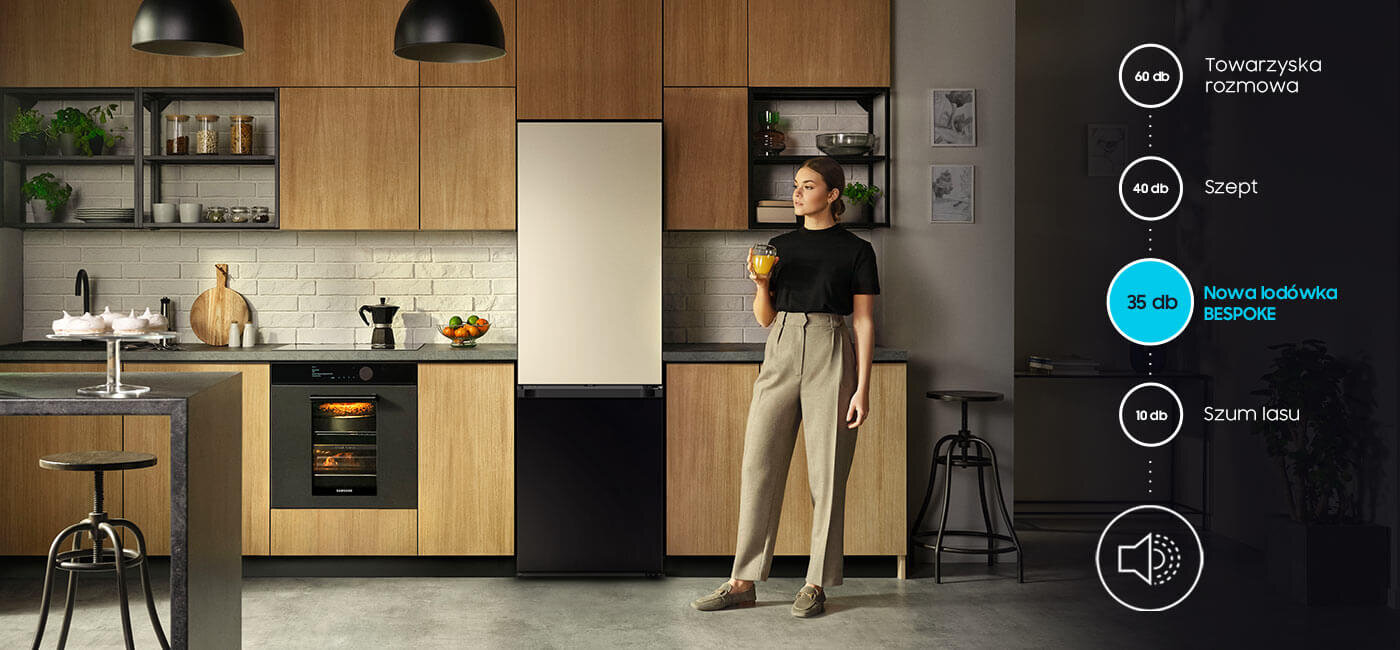Natężenie dźwięku lodówki Samsung Bespoke w porównaniu do innych odgłosów Kobieta stoi w nowoczesnej kuchni obok lodówki bez panelu, trzymając szklankę z napojem. Po prawej stronie widoczna jest grafika z poziomami hałasu: \'Towarzyska rozmowa 60 db\', \'Szept 40 db\', \'Nowa lodówka BESPOKE 35 db\', \'Szum lasu 10 db\'.