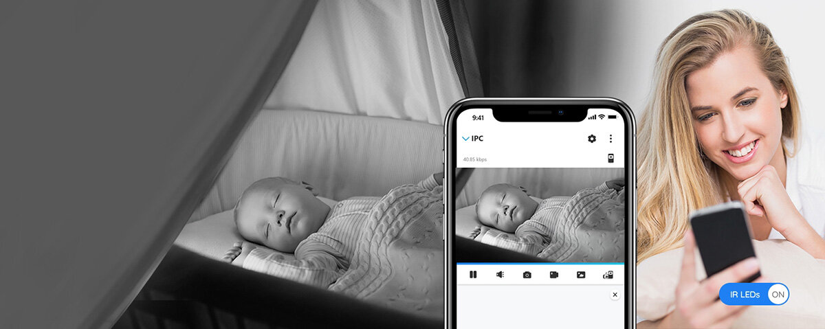 Obraz przedstawia kobietę trzymającą smartfon z wyświetlonym obrazem dziecka śpiącego w łóżeczku. Na ekranie telefonu widoczny jest interfejs aplikacji monitorującej z napisem \'IPC\'.