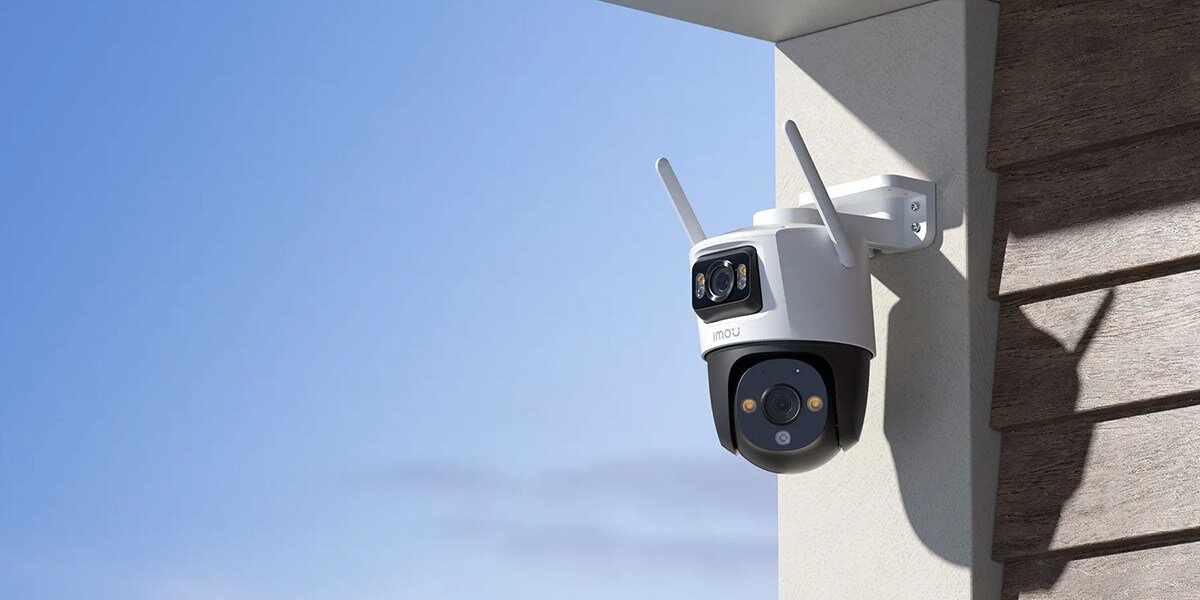 Na obrazie widoczna jest zewnętrzna kamera monitoringu zamontowana na ścianie budynku. Kamera ma biały korpus z dwoma antenami i logo \'imou\'.