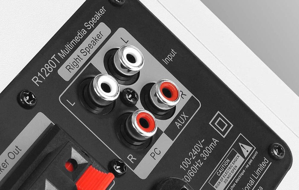 Zdjęcie przedstawia panel tylni głośnika z oznaczeniami \'R1280T Multimedia Speaker\' oraz wejściami RCA oznaczonymi jako \'L\' i \'R\' dla \'PC\' i \'AUX\'. Widoczna jest również informacja o zasilaniu: \'100-240V~ 50/60Hz 300mA\'.
