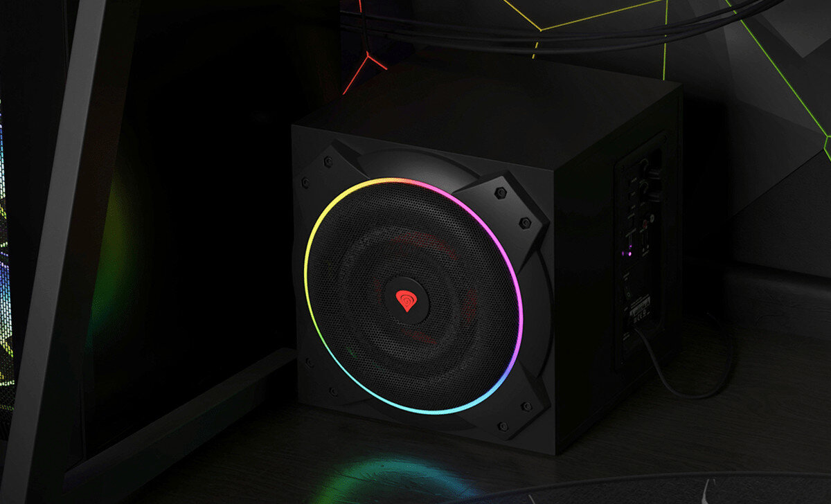 Czarny subwoofer z podświetleniem LED w różnych kolorach, umieszczony w rogu pomieszczenia. Na przednim panelu widoczne jest logo w kształcie czerwonego trójkąta.