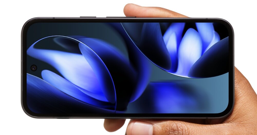 Osoba trzyma smartfon z wyświetlaczem pokazującym abstrakcyjny, niebiesko-czarny wzór. Telefon ma cienkie ramki i przednią kamerę umieszczoną centralnie u góry ekranu.