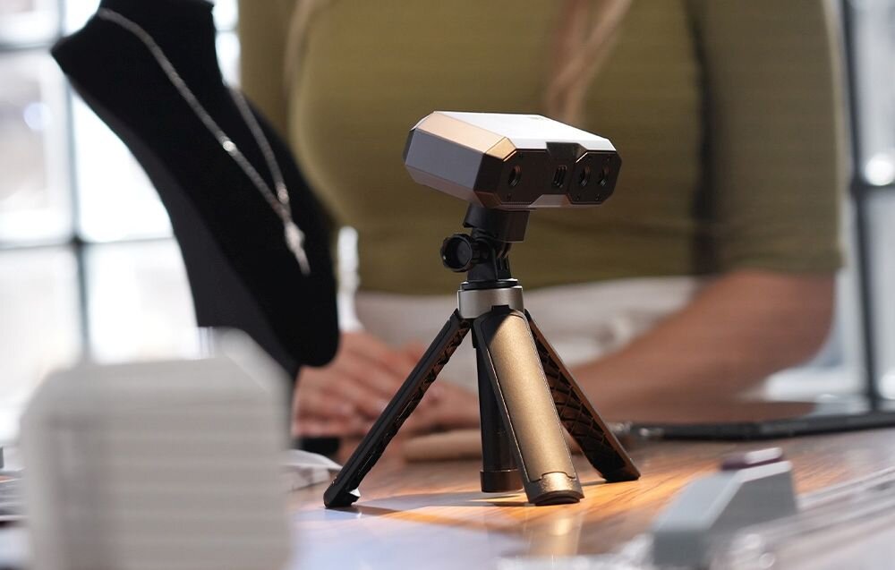 Skaner 3D Revopoint Mini Mini z niebieskim światłem na trójnogu na biurku z matą w kropki