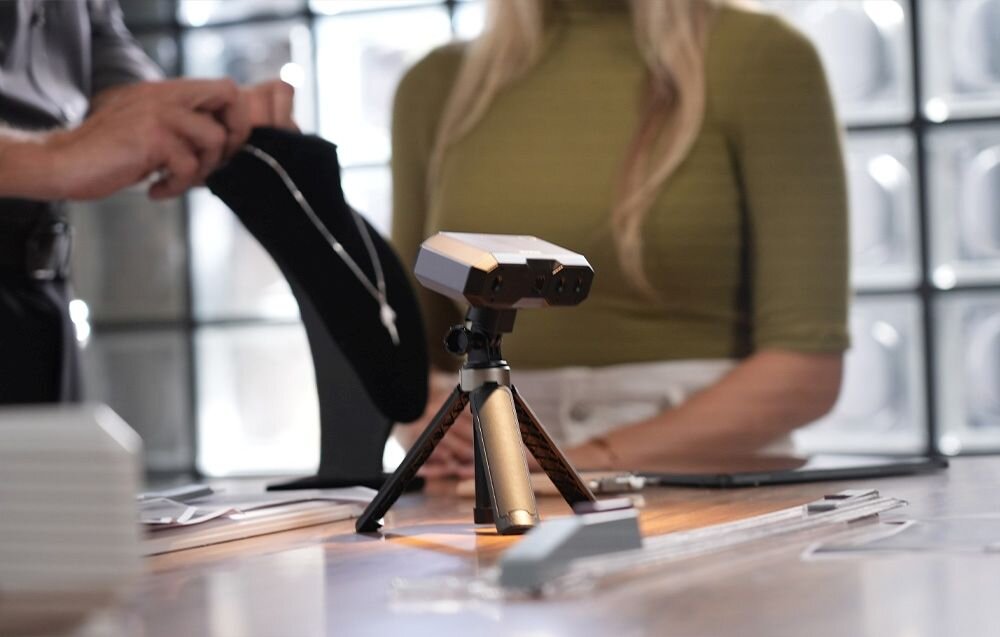 Skaner 3D Revopoint Mini Mini z niebieskim światłem na trójnogu na biurku z matą w kropki