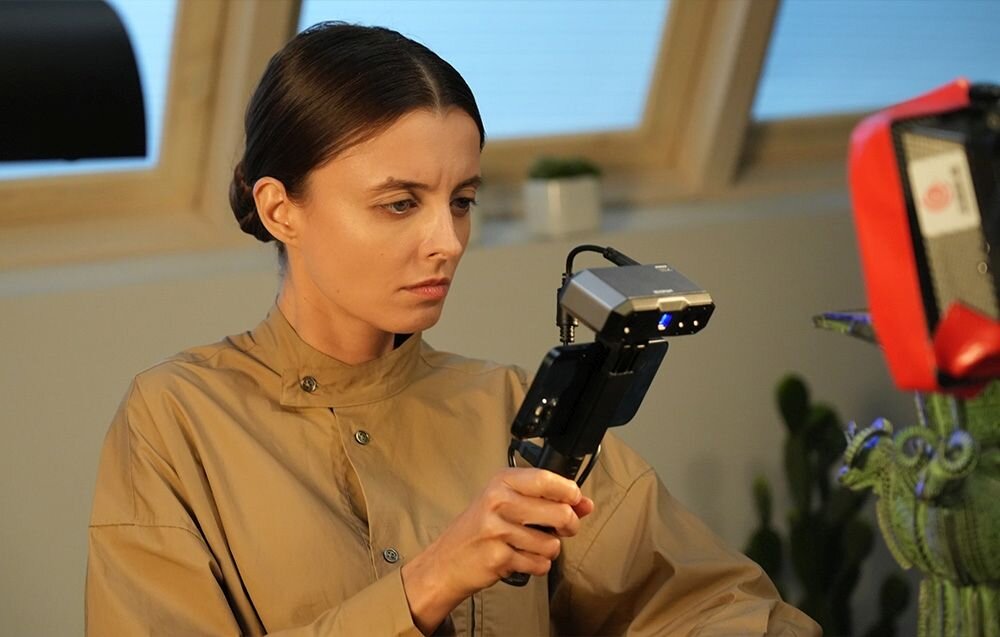 Skaner 3D Revopoint Mini Mini z niebieskim światłem na trójnogu na biurku z matą w kropki