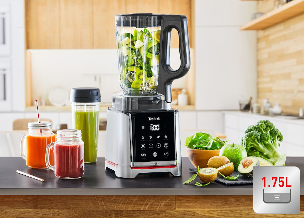 Na blacie kuchennym stoi blender kielichowy z logo Tefal, wypełniony zielonymi składnikami. Obok znajdują się dwa słoiki z sokami, zielony bidon oraz świeże warzywa i owoce; w rogu widnieje napis \'1.75L\'.