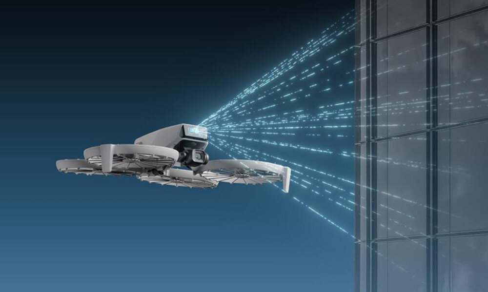 Dron unosi się w powietrzu przed szklaną powierzchnią, emitując niebieskie linie świetlne w kierunku budynku. Tło jest ciemnoniebieskie, co podkreśla futurystyczny wygląd sceny.