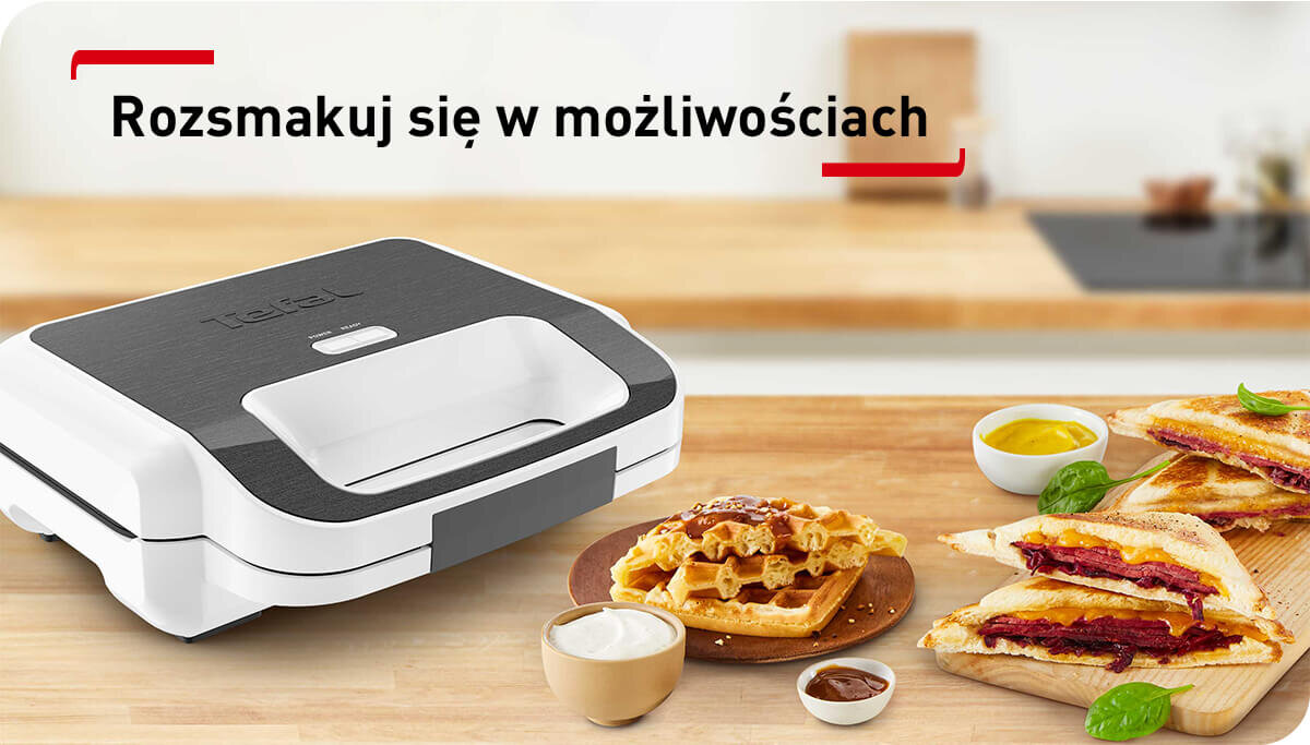 Na drewnianym blacie kuchennym znajduje się opiekacz z logo TEFAL oraz talerze z goframi i tostami. W tle widoczny jest napis \'Rozsmakuj się w możliwościach\'.