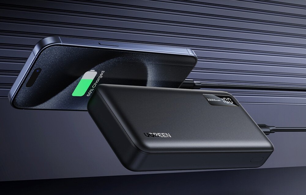 Powerbank UGREEN PB312 20000 mAh funkcję Pass-through równocześnie ładować jego akumulator oraz podłączone urządzenia Maksymalna moc ładowania 15 W - Smartfon ładowany za pomocą kabla podłączonego do leżącego obok powerbanku Ugreen z wyświetlaczem 100%.