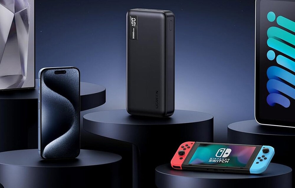 Powerbank UGREEN PB312 20000 mAh 20 000 mAh torbie, plecaku czy bagażu podręcznym 147 x 71,6 x 27,7 mm - Powerbank Ugreen stojący obok smartfona, konsoli Nintendo Switch oraz tabletu na ciemnoniebieskich podestach.