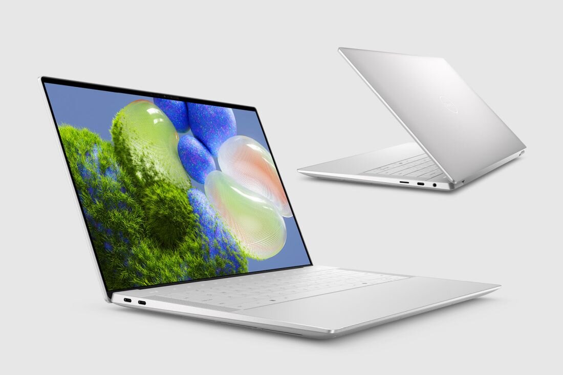 Na obrazie widoczne są dwa laptopy w kolorze srebrnym, jeden otwarty z wyświetlaczem pokazującym kolorową grafikę, drugi zamknięty z widocznym logo producenta. Laptopy mają smukłą konstrukcję i nowoczesny design.