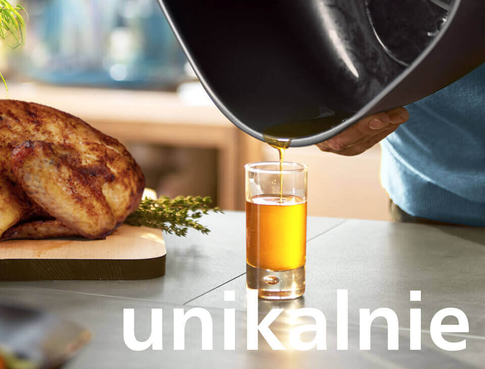Osoba nalewa płyn z czarnego naczynia do szklanki, obok leży pieczone mięso na desce. Na dole obrazu widoczny jest napis \'unikalnie\'.