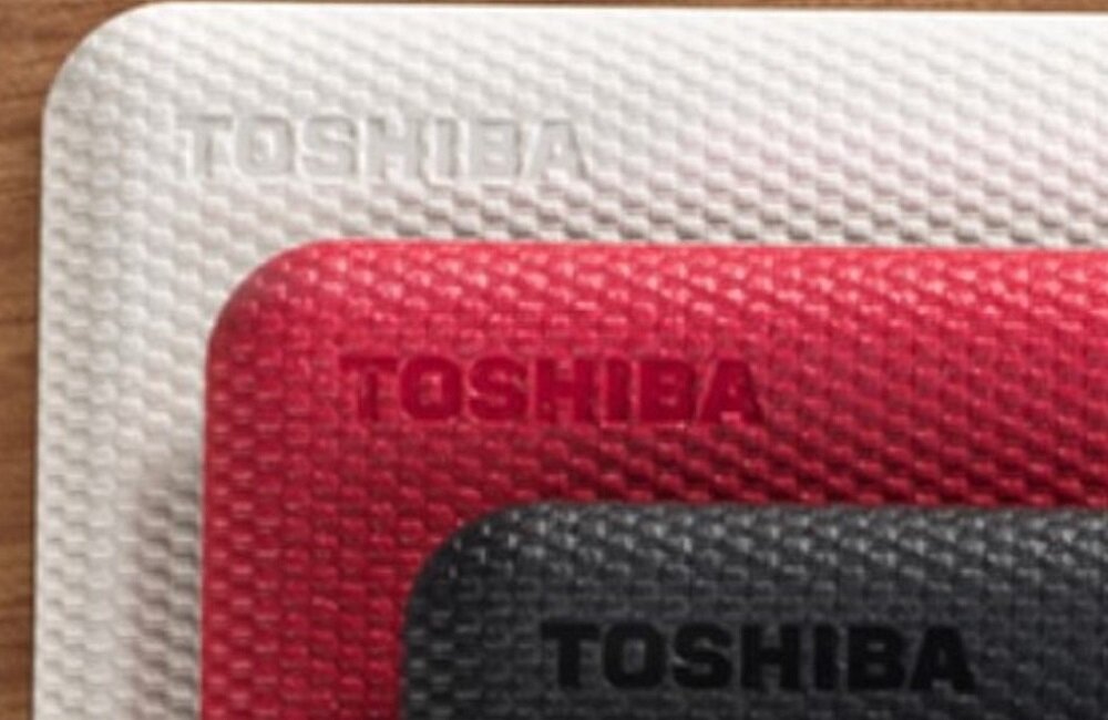 Obraz przedstawia trzy dyski z teksturą, ułożone jeden na drugim w kolorach białym, czerwonym i czarnym, z widocznym napisem \'TOSHIBA\' na każdym z nich.