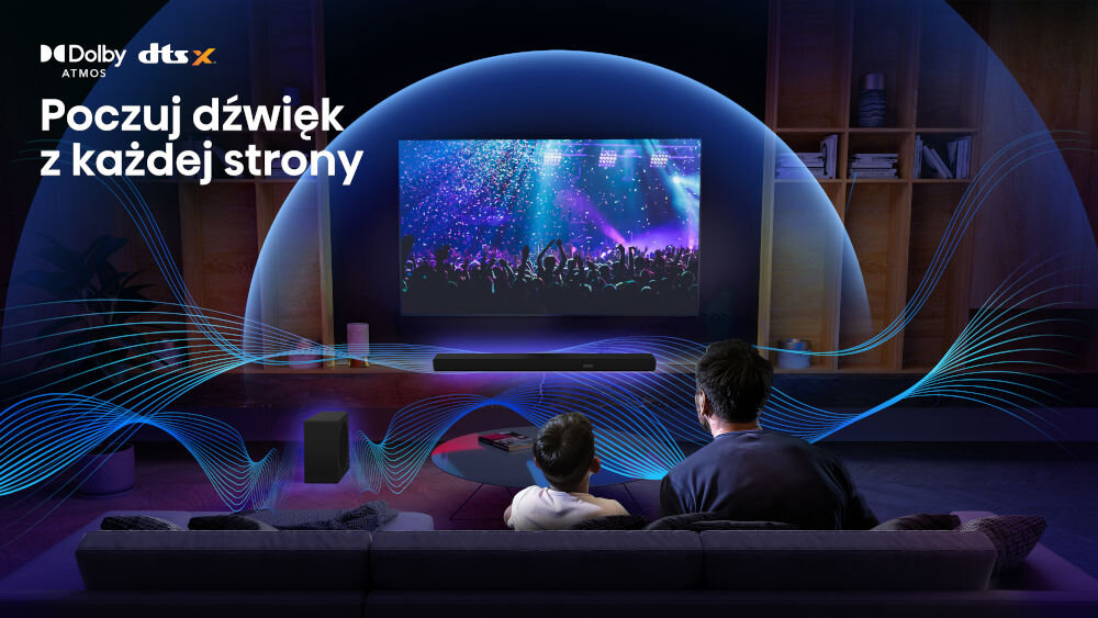 Na obrazie widać dwie osoby siedzące na kanapie przed telewizorem, na którym wyświetlany jest koncert. W górnym lewym rogu znajdują się loga Dolby Atmos i DTS:X oraz tekst \'Poczuj dźwięk z każdej strony\'.