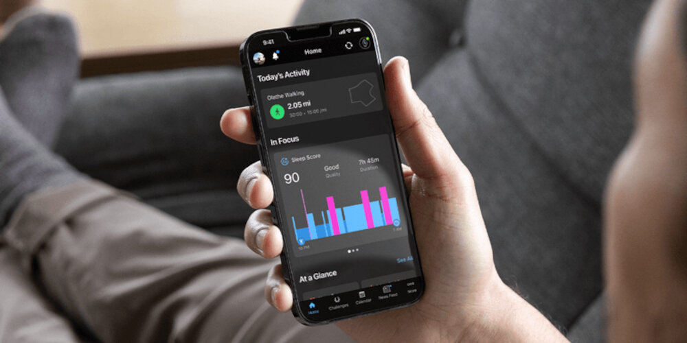 Osoba trzyma smartfon z aplikacją wyświetlającą dane aktywności fizycznej, w tym dystans i wykresy. Na ekranie widoczny jest tekst: \'Today\'s Activity\', \'In Focus\', \'Sleep Score 90\'.