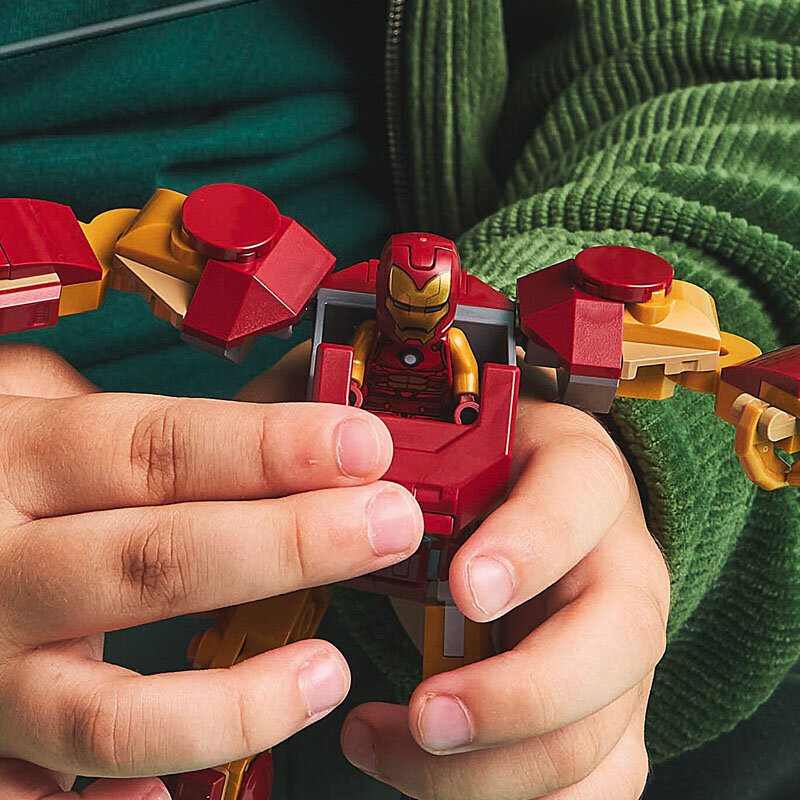 Dziecko trzyma figurkę LEGO przedstawiającą postać w czerwono-złotej zbroi. Figurka ma ruchome elementy i siedzi w większym mechaniźmie.