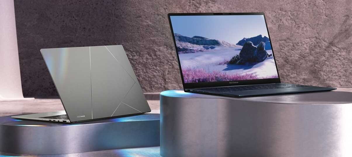 Dwa laptopy na cylindrycznych podestach, jeden otwarty z widocznym ekranem, drugi zamknięty z widocznym logo ASUS. W tle znajduje się kamienna ściana.