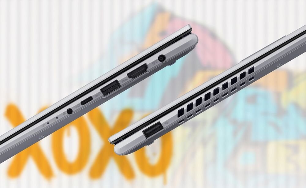 Obraz przedstawia dwa laptopy w pozycji zamkniętej, ukazujące porty boczne i otwory wentylacyjne. W tle widoczny jest kolorowy napis \'XOXO\'.