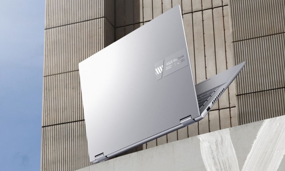 Srebrny laptop z widocznym logo i napisem \'ASUS VivoBook\' na pokrywie, ustawiony na tle betonowej struktury.