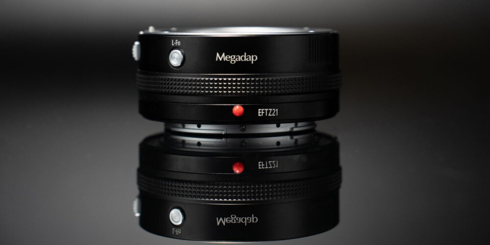 ADAPTER BAGNETOWY Z AUTOFOCUSEM MEGADAP EFTZ21 - CANON EF NIKON Z Czarny adapter bagnetowy z widocznym przyciskiem i oznaczeniem modelu ustawiony na błyszczącej powierzchni, na ciemnym tle