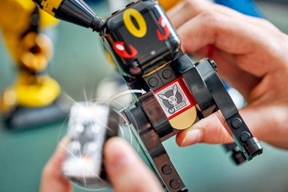 Osoba trzyma model z klocków LEGO przedstawiający postać z dużymi uszami i żółtym symbolem na głowie. Na modelu widoczny jest nadruk z napisem \'HOBBY\'.