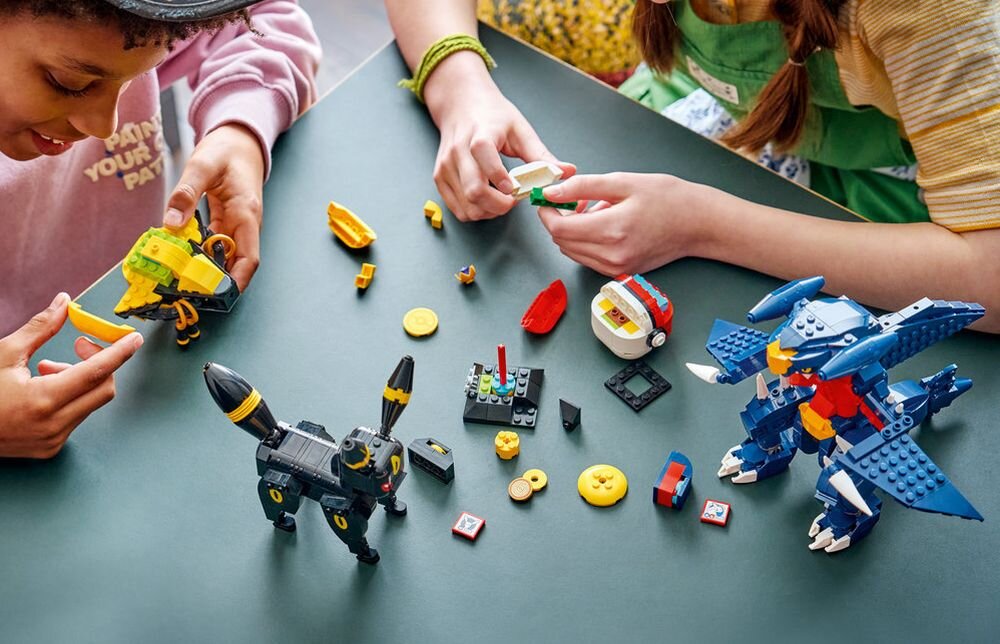 Na stole znajdują się klocki LEGO, w tym modele przypominające postacie Umbreon i Garchomp. Dwie osoby bawią się klockami, składając różne elementy.