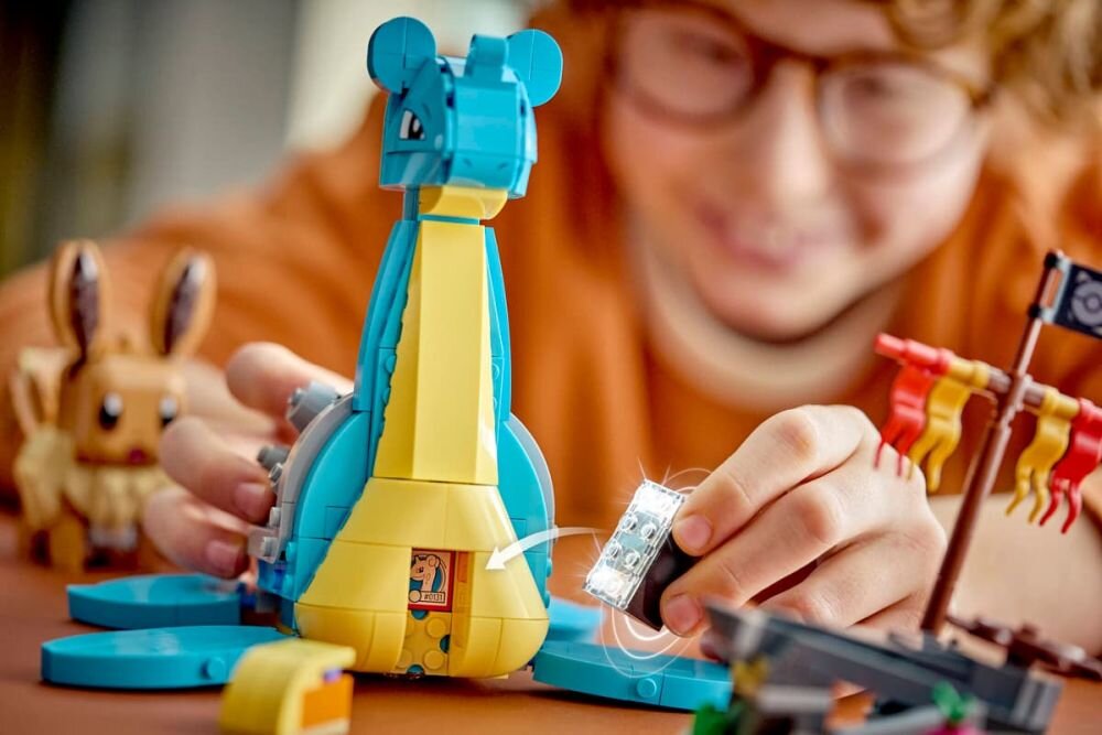 Na obrazie widać zestaw LEGO przedstawiający postać Laprasa z serii Pokémon oraz Eevee w tle. Dziecko bawi się klockami, trzymając element z przezroczystymi klockami, a na Laprasie widoczny jest mały ekran z grafiką.