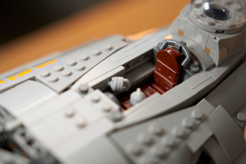 Крупний план моделі LEGO з кабіною винищувача з сидінням та органами керування. Видно деталі конструкції з сірої та червоної цегли.