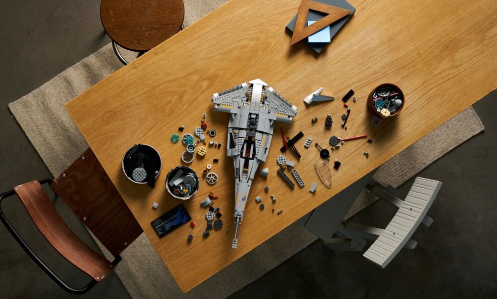 На дерев'яному столі виставлені деталі LEGO, зокрема деталі, з яких складається модель винищувача. Поруч із ними стоять миски з додатковими цеглинами та геометричні інструменти.