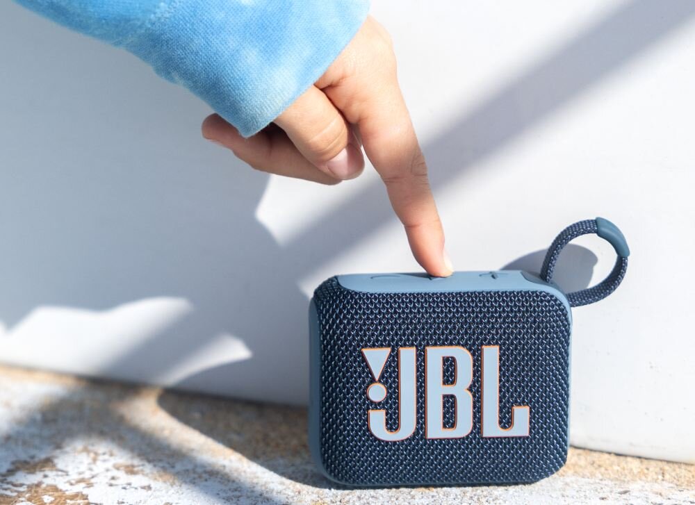 Osoba dotyka niebieskiego głośnika przenośnego z widocznym logo \'JBL\'.