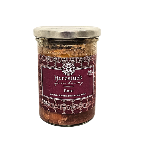 Słoik z metalową pokrywką, zawierający produkt spożywczy. Etykieta w kolorze bordowym z białym napisem: \'Herzstück fine dining Ente mit Reis, Karotte, Banane und Kokos\'.