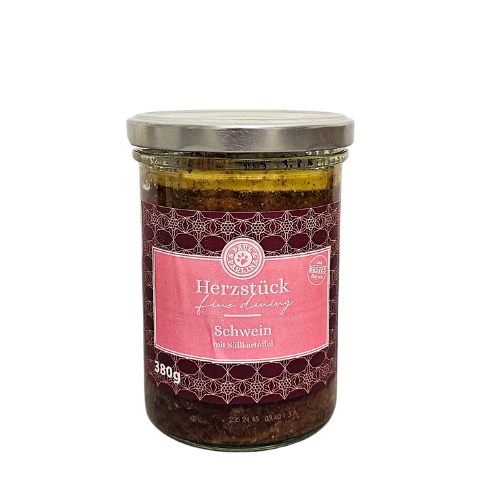Słoik z metalową pokrywką zawiera produkt oznaczony etykietą z napisem \'Herzstück fine dining Schwein mit Süßkartoffel 380g\'. Etykieta jest różowa z ozdobnym wzorem i logo producenta.