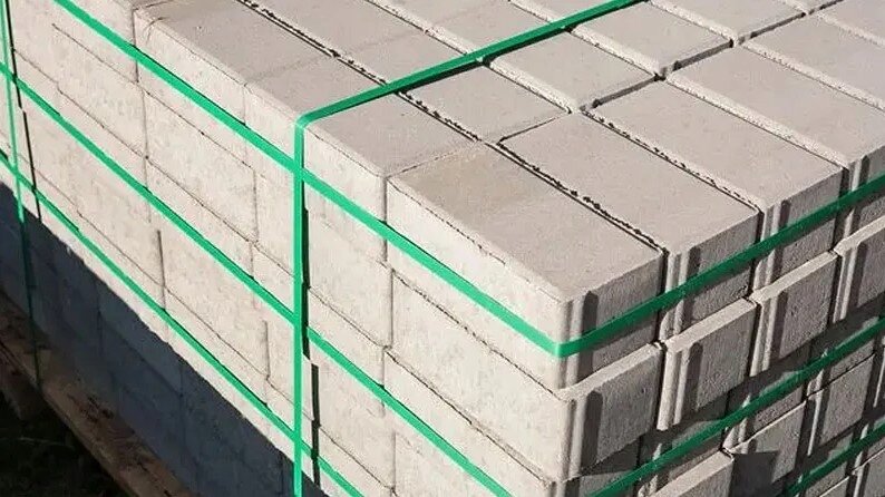 Stos betonowych bloczków owinięty zieloną taśmą do bandowania. Taśma jest napięta wokół palety, zabezpieczając ładunek.