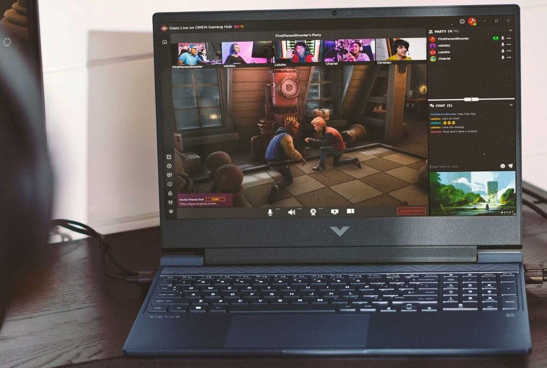Laptop z otwartym ekranem, na którym wyświetlana jest gra oraz okna czatu wideo. Na obudowie widoczne jest logo w kształcie litery V.