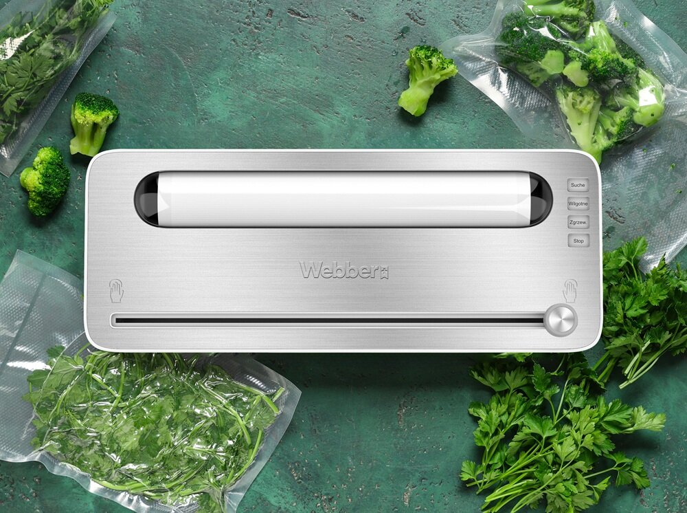 Na obrazie znajduje się zgrzewarka próżniowa z napisem \'Webber\' na metalicznej obudowie. Wokół urządzenia widoczne są zapakowane próżniowo warzywa, takie jak brokuły i zioła.