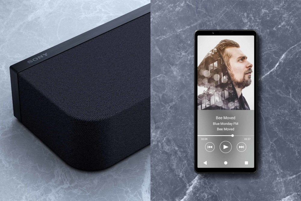 Po lewej stronie widoczny jest czarny soundbar z logo \'SONY\' na górnej krawędzi. Po prawej stronie znajduje się smartfon z wyświetlaczem pokazującym odtwarzacz muzyki z utworem \'Bee Moved\' i zdjęciem mężczyzny.