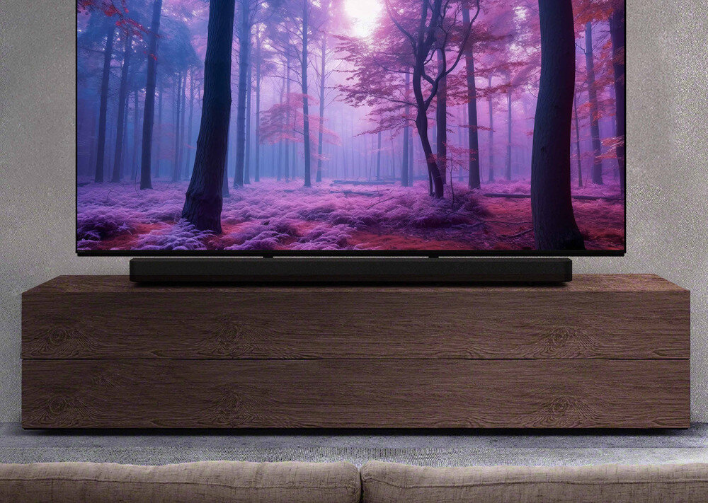 Na drewnianej szafce stoi telewizor z wyświetlonym obrazem lasu w odcieniach fioletu i różu. Przed telewizorem znajduje się czarny soundbar.