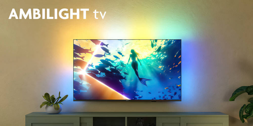Telewizor wyświetla kolorowy obraz z syreną pod wodą, a na ścianie wokół niego widoczne są efekty świetlne. W lewym górnym rogu znajduje się napis \'AMBILIGHT tv\'.