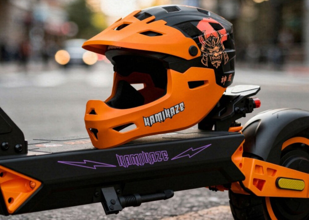 Pomarańczowy kask full face z napisem \'KAMIKAZE\' i grafiką samuraja, umieszczony na hulajnodze z widocznym logo \'KAMIKAZE\'.