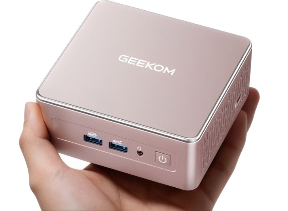 Komputer GEEKOM A5 Dłoń trzymająca mały, kwadratowy komputer stacjonarny z widocznymi portami USB, gniazdem audio i przyciskiem zasilania na przedniej ściance