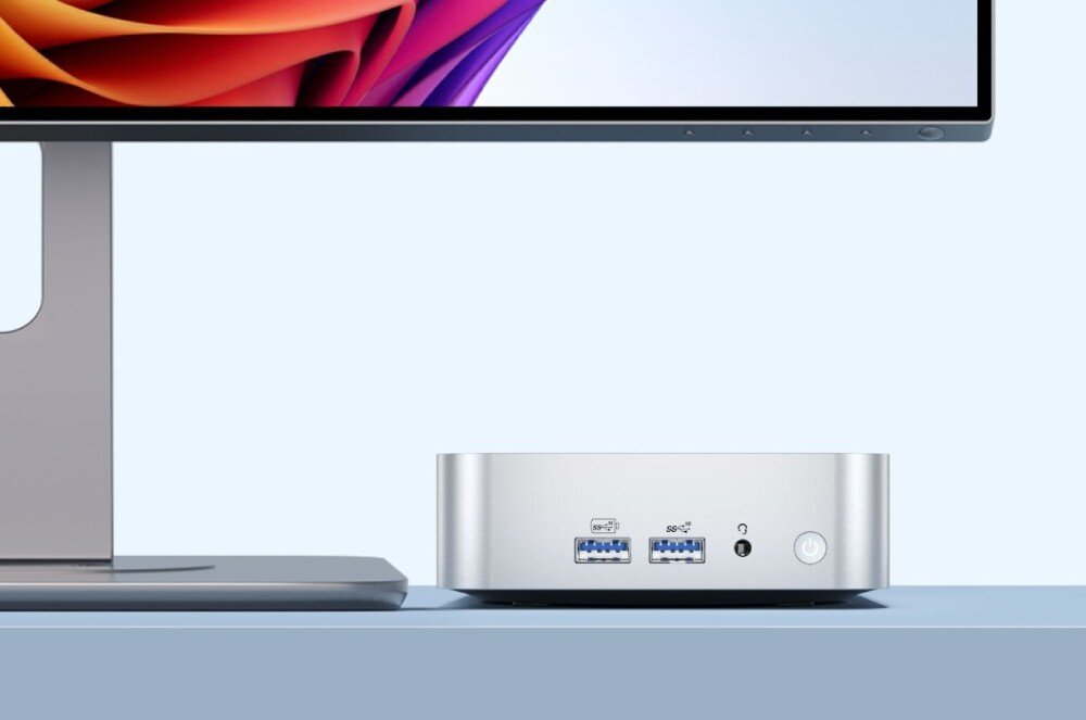 Komputer GEEKOM A6 Przedni panel minikomputera z portami USB, gniazdem audio i włącznikiem, stojący obok monitora