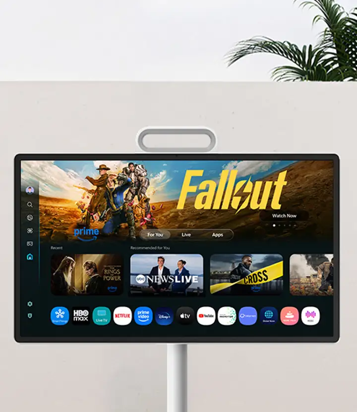 Telewizor wyświetla ekran główny z aplikacjami streamingowymi, na którym widoczny jest plakat z napisem \'Fallout\'. W tle znajduje się jasna ściana i roślina.