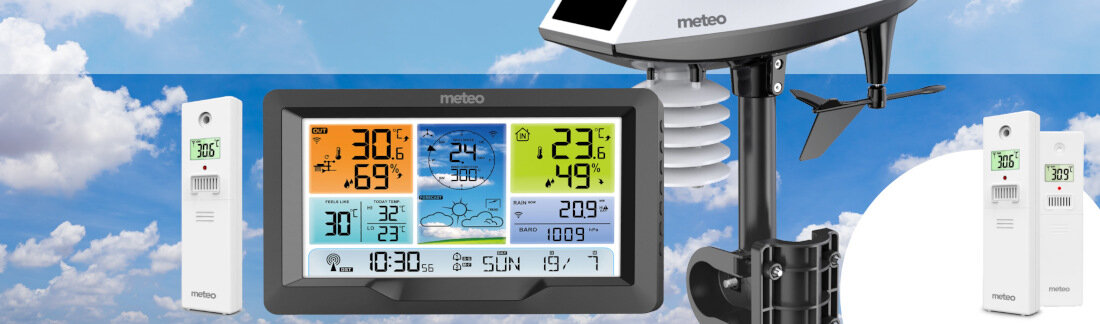 Obraz przedstawia stację pogody z wyświetlaczem pokazującym różne dane meteorologiczne, takie jak temperatura, wilgotność i ciśnienie. W tle widoczne są chmury, a na urządzeniach znajduje się logo \'meteo\'.