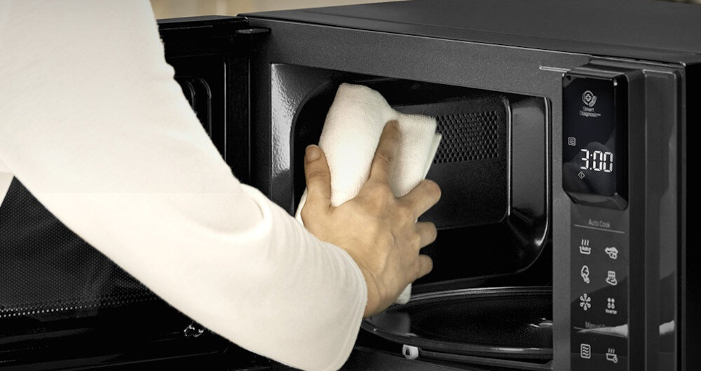 KUCHNIA MIKROFALOWA LG MS23NECBW Osoba przeciera miękką ściereczką wnętrze kuchenki mikrofalowej LG NeoChef, otwartą od frontu, co podkreśla łatwe i wygodne czyszczenie gładkiej komory urządzenia.