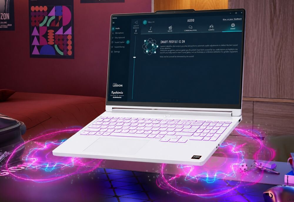 Na obrazie znajduje się biały laptop z podświetlaną klawiaturą, na ekranie widoczny jest interfejs oprogramowania audio z napisem \'SMART PROFILE IS ON\'. W tle znajduje się pokój z plakatami na ścianie, a na biurku leży kilka przedmiotów.