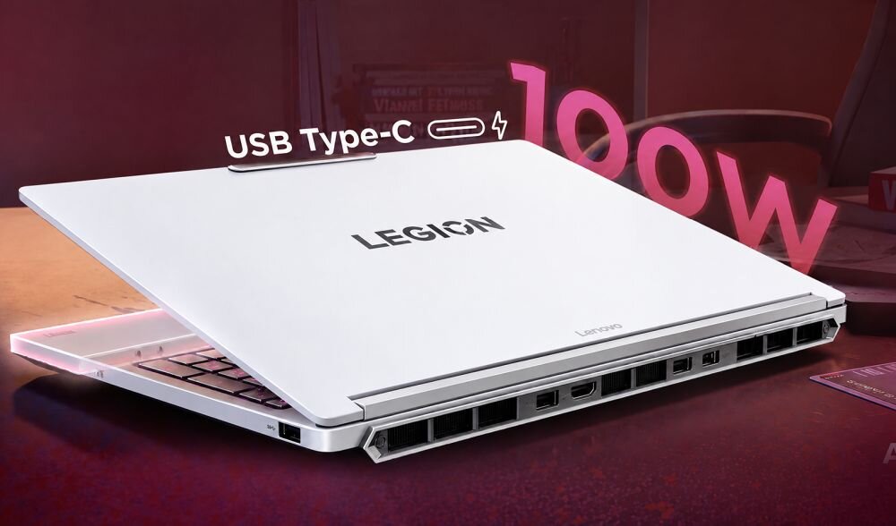 Na obrazie widoczny jest biały laptop z napisem \'LEGION\' na pokrywie, z otwartym ekranem i widocznymi portami z tyłu. Nad laptopem znajduje się napis \'USB Type-C\' oraz liczba \'100W\'.