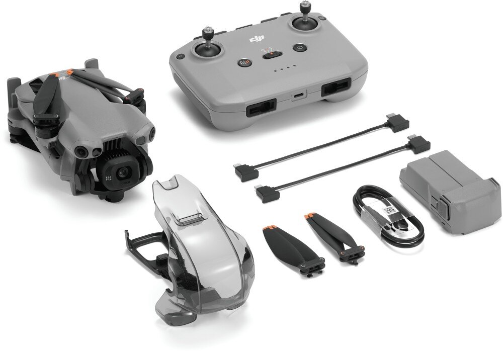 Na obrazie znajduje się szary dron złożony obok kontrolera, dwóch kabli, baterii, dwóch śmigieł i kabla USB. Na kontrolerze widoczne jest logo DJI.