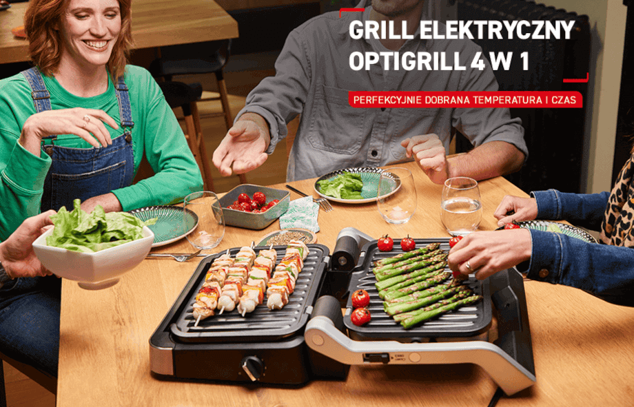 Na stole znajduje się grill elektryczny z grillowanymi szaszłykami i szparagami. Obok widoczny jest napis: \'GRILL ELEKTRYCZNY OPTIGRILL 4 W 1 PERFEKCYJNIE DOBRANA TEMPERATURA I CZAS\'.