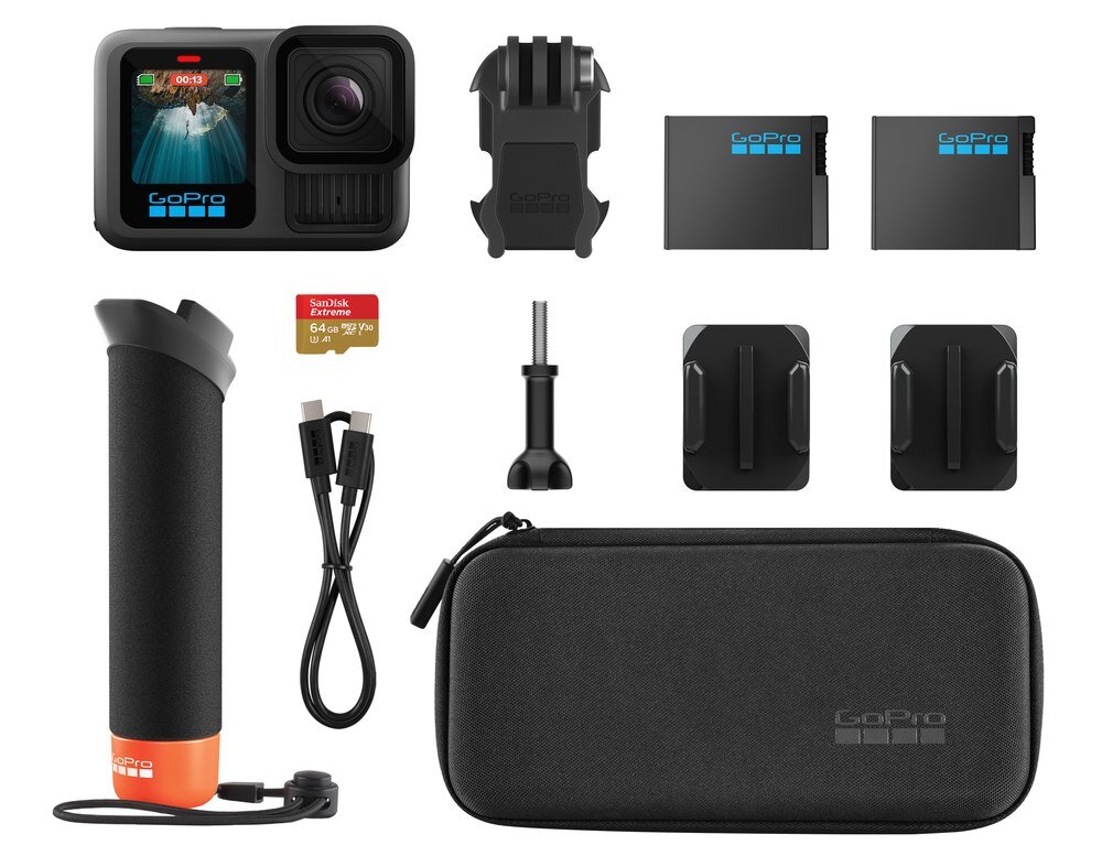 Na obrazie znajduje się zestaw akcesoriów do kamery sportowej, w tym kamera z wyświetlaczem, dwa akumulatory, uchwyt, karta pamięci SanDisk 64 GB, kabel USB, etui oraz kilka mocowań. Na kamerze i etui widoczne jest logo GoPro.