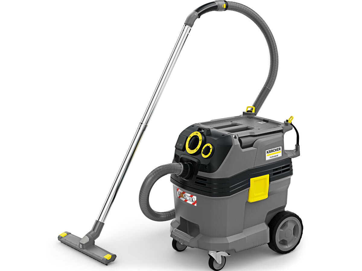 Na obrazie widoczny jest odkurzacz przemysłowy w kolorze szaro-żółtym z logo \'KARCHER\' na boku. Odkurzacz ma duże koła i długi metalowy wąż zakończony ssawką.